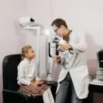 Eye doctor examining a young girl in a clinic setting with ophthalmological equipment.